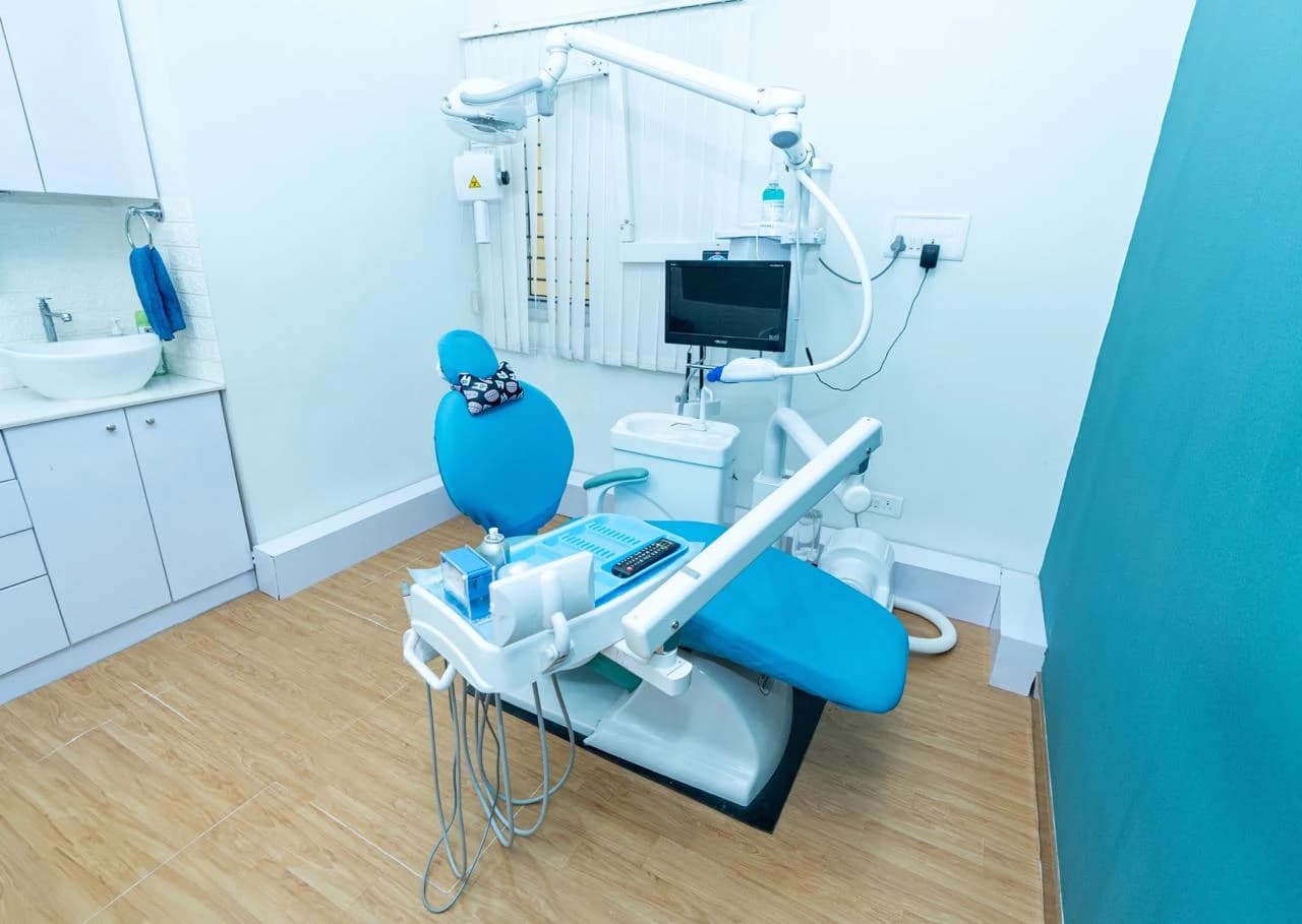Dental operatory with blue treatment chair, monitor, and clean cabinetry at Bangalore Smiles