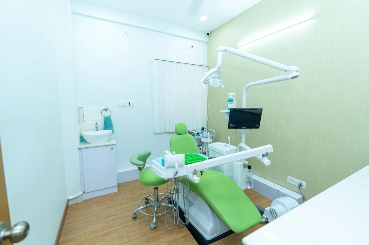 Dental operatory with green treatment chair, examination light, and washbasin at Bangalore Smiles in Hegde Nagar